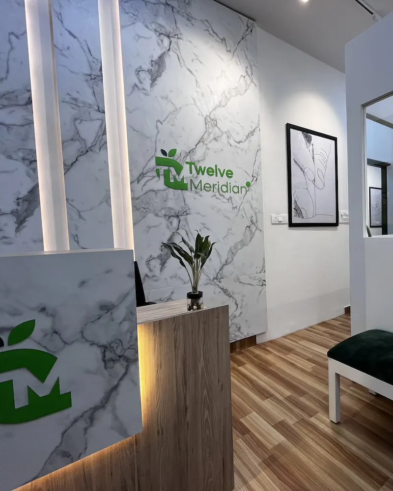 Reception at Twelve Meridian, Sector 11, Noida: marble wall with the Twelve Meridian logo, front desk and waiting bench