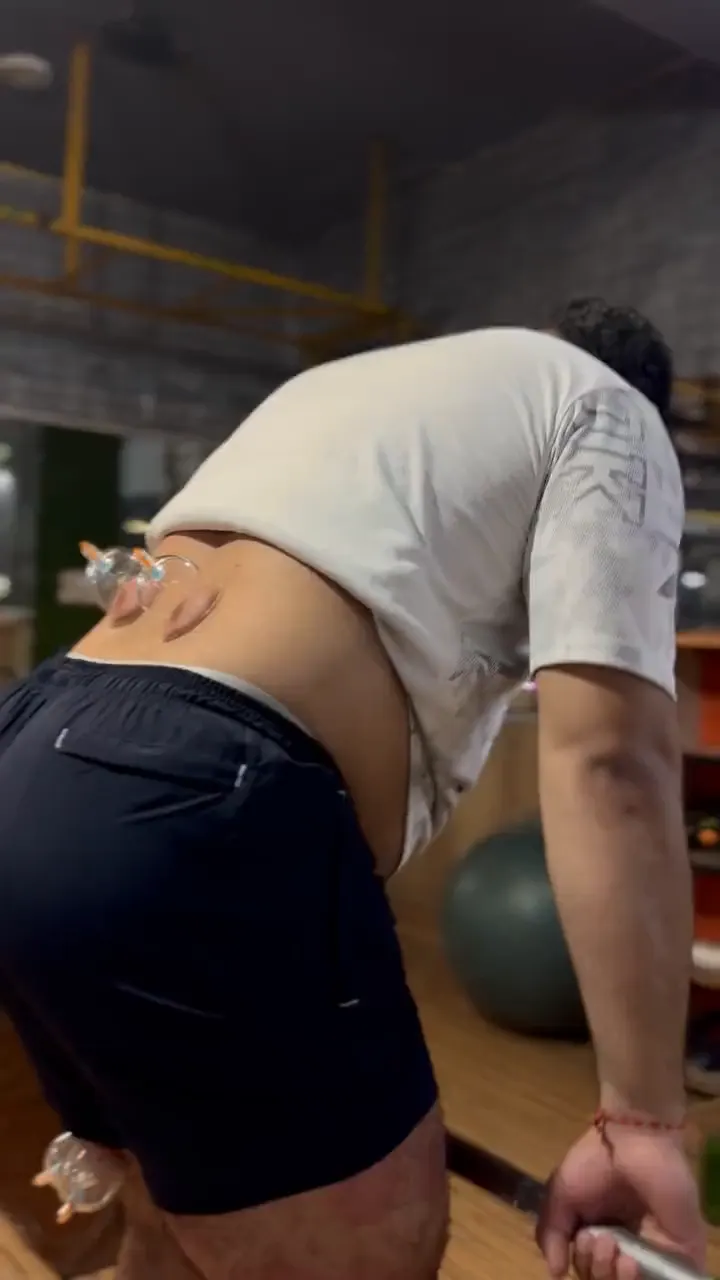 Man in a gym with cups on his lower back, bending forward into a hip hinge