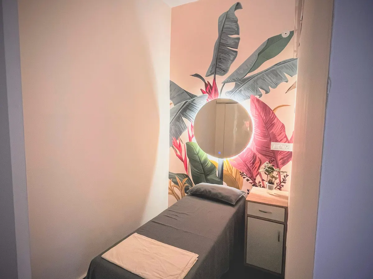 A session room at Twelve Meridian: a session bed against a mural wall, with a mirror and side table